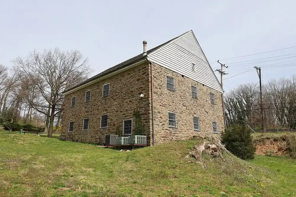 Historic stone Adelphi Mill on a grassy rise beneath bare trees in Adelphi, Maryland