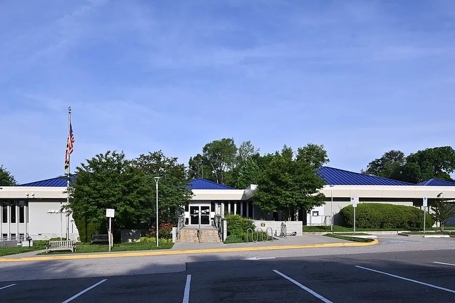 Blue-roofed public library with a flagpole and leafy trees in Aspen Hill, Maryland