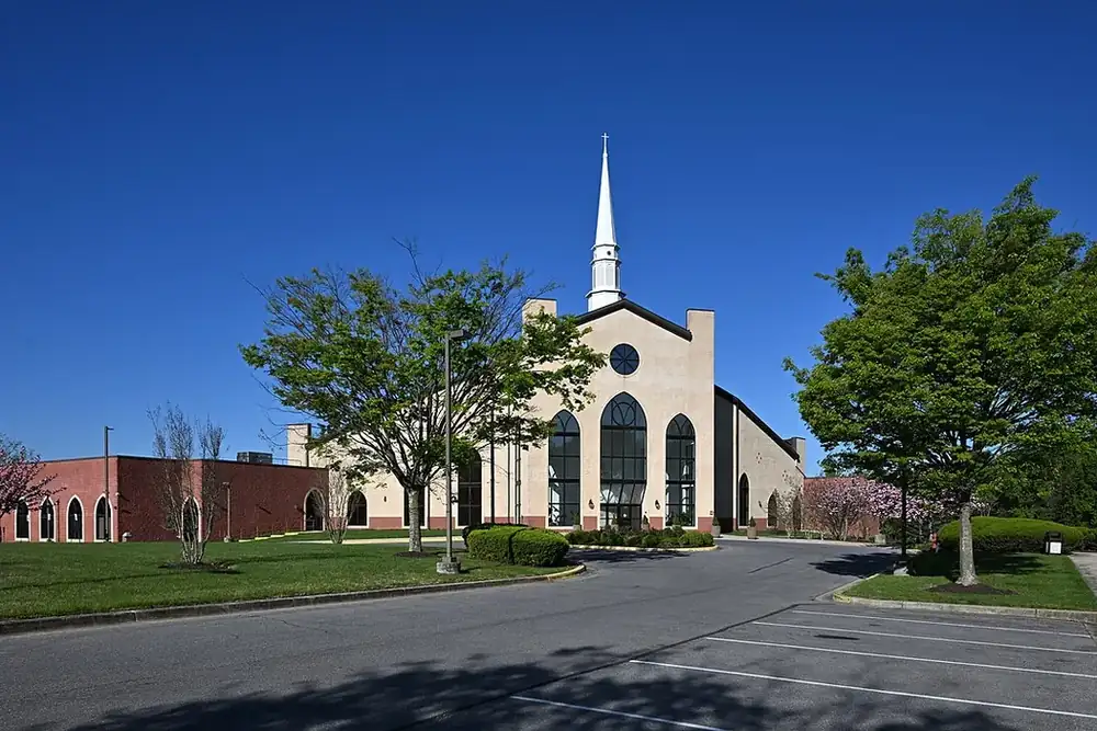White-steepled Southern Asian Seventh-day Adventist Church behind leafy trees in Fairland, Maryland