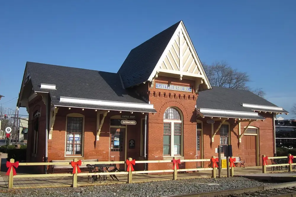 Historic red-brick railroad station with a steep gabled roof beside the tracks in Gaithersburg, Maryland