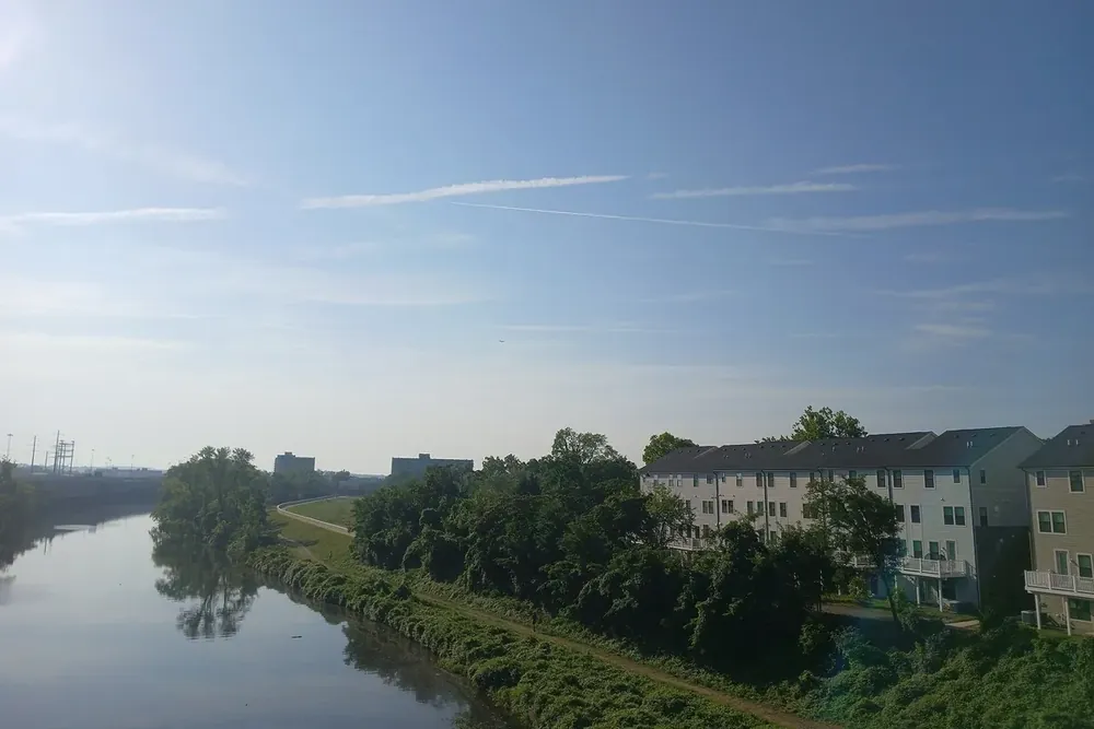 Cameron Run creek with a trail and townhouses under a hazy morning sky in Huntington, Virginia