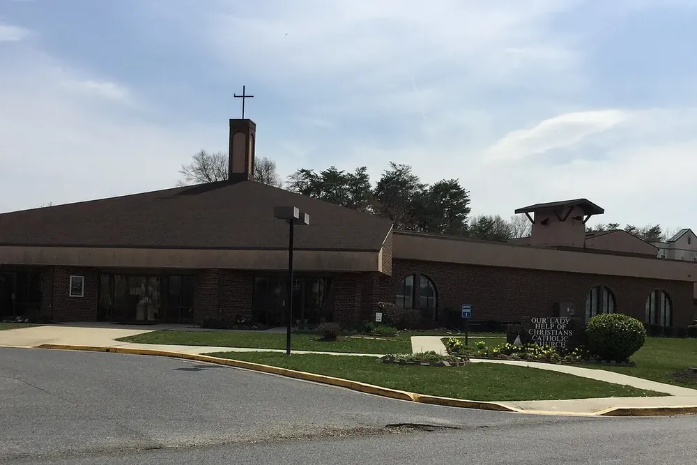 Low brick Our Lady Help of Christians church with a cross tower and lawn in Waldorf, Maryland